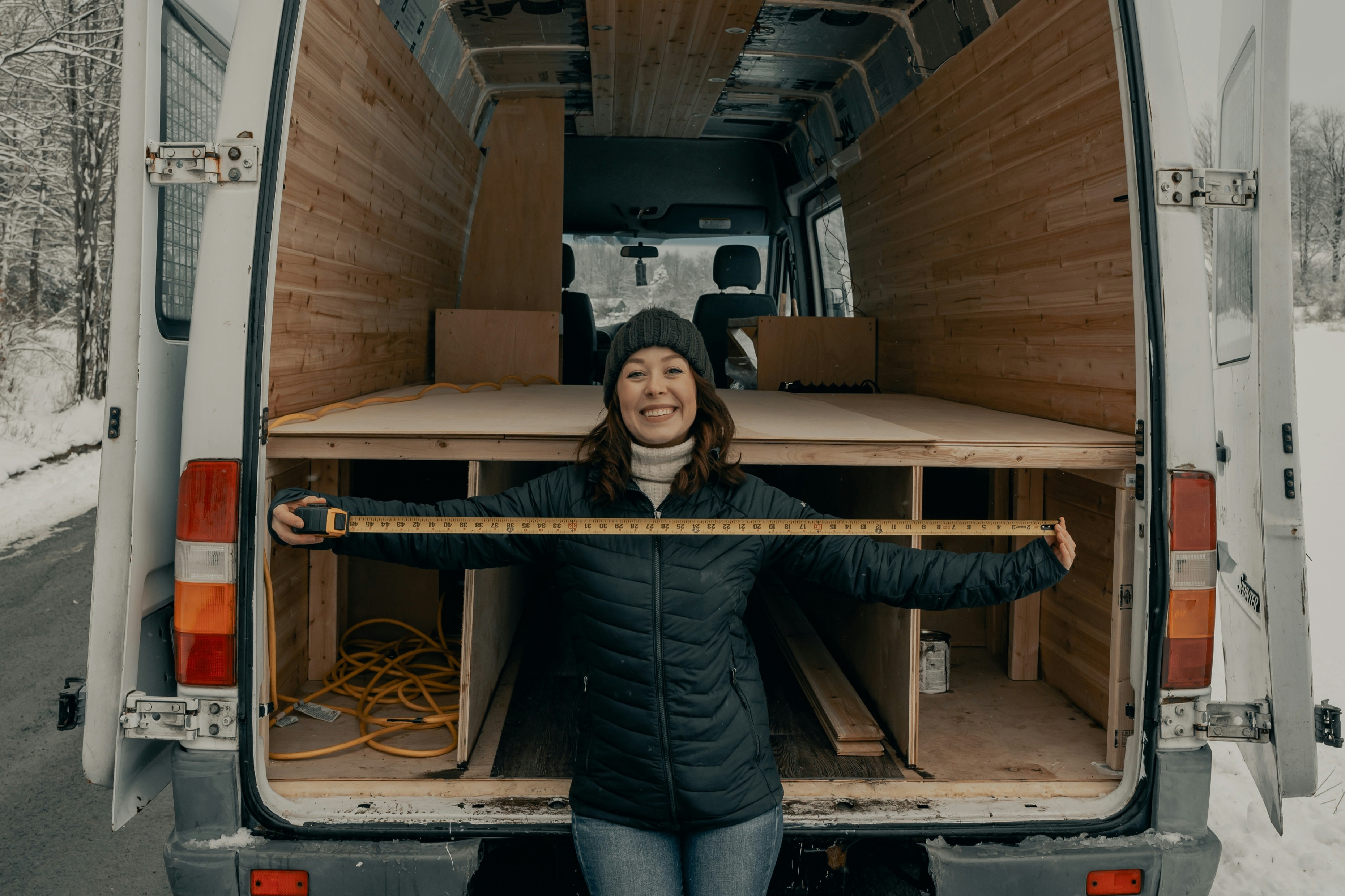 Wanda holding up a measuring tape at the back of her van smiling